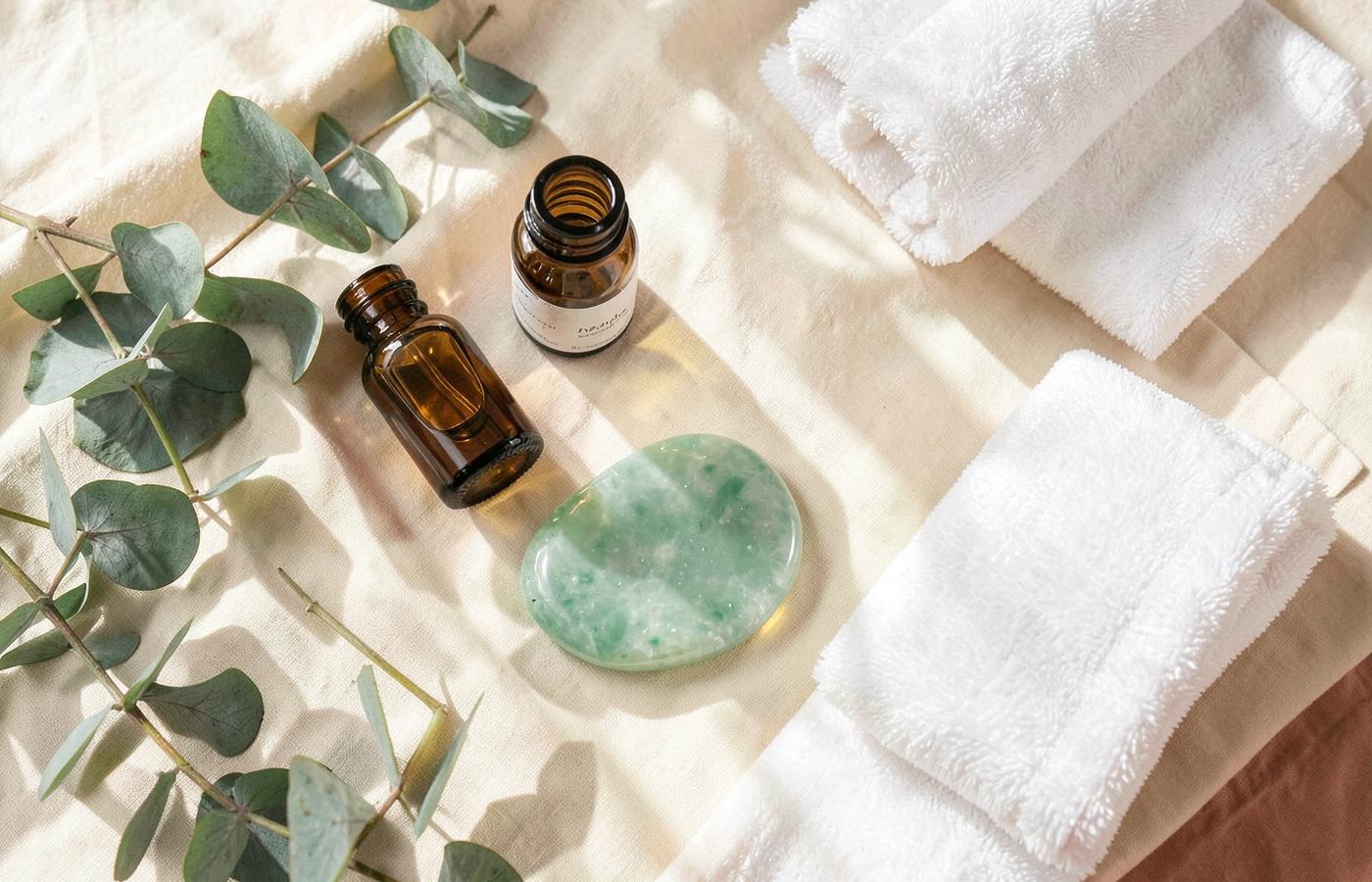 Skincare products, gua sha stone, and towels arranged on cream linen